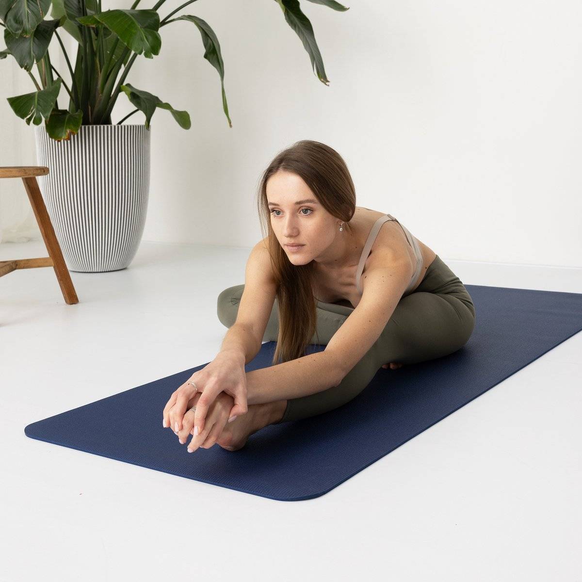 a woman sitting on a yoga mat in a white room